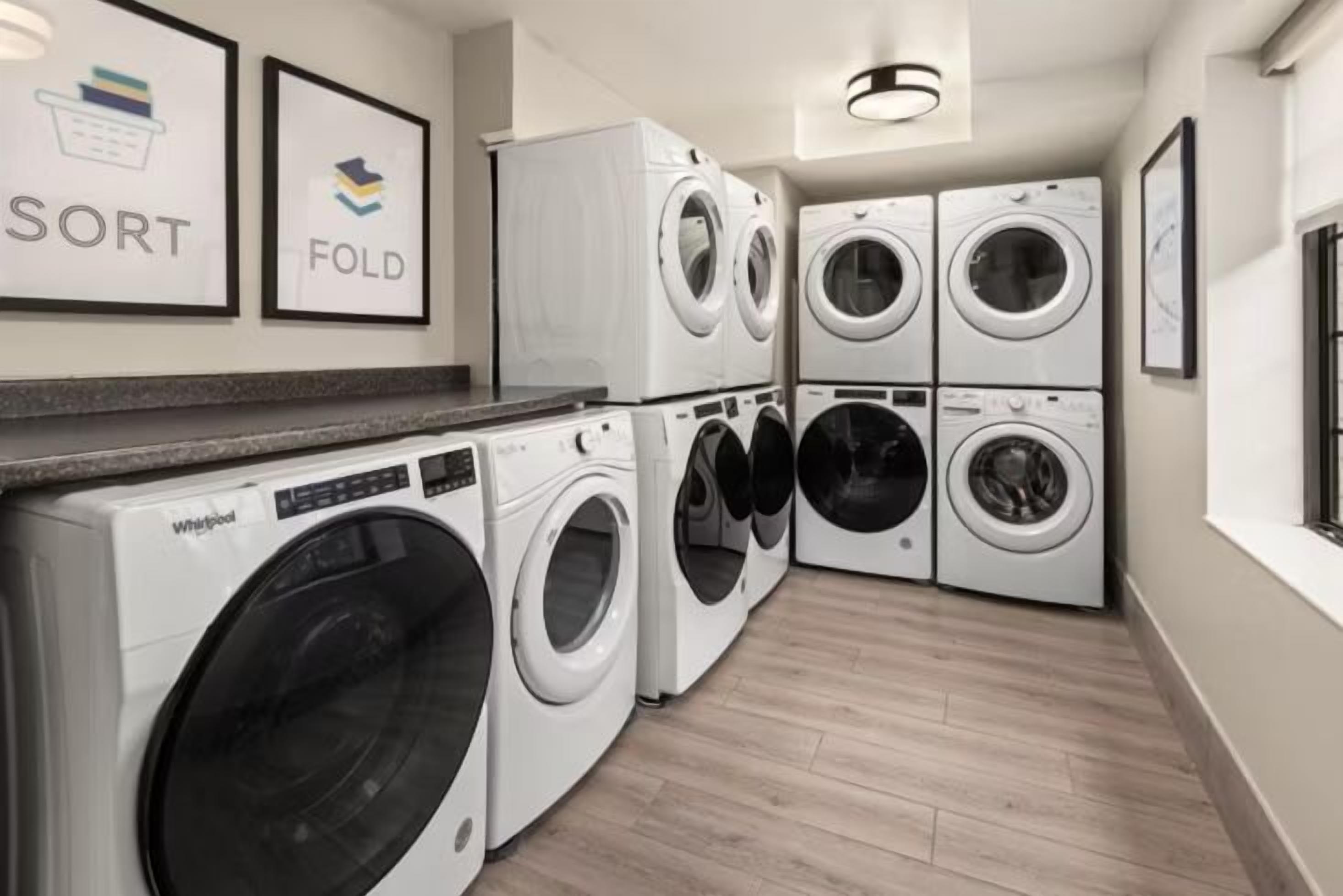 A laundry room with stacked washers and dryers, a countertop, and framed wall art.