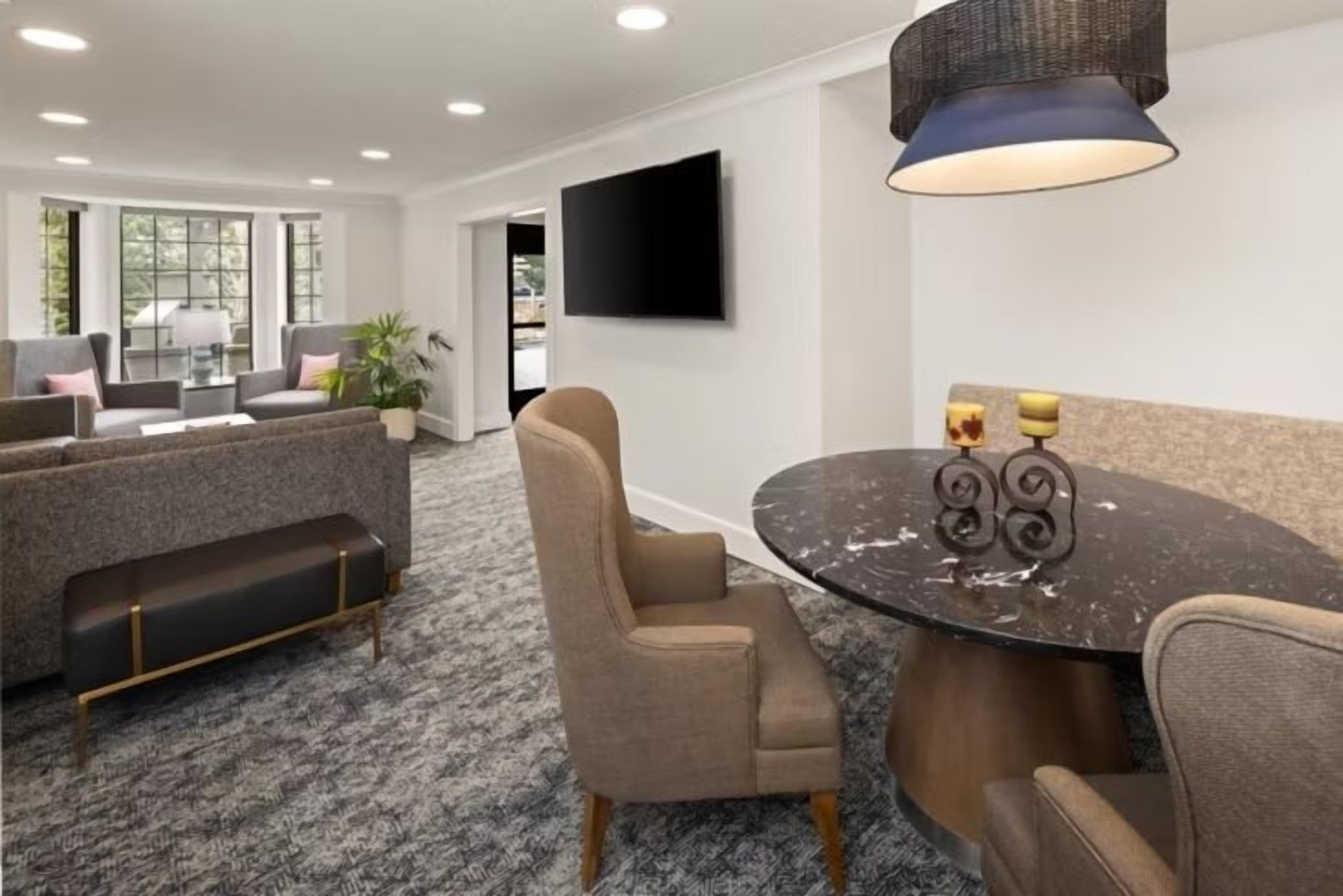 A modern hotel room with a sofa set, a round table with candles, and a flat-screen TV mounted on the wall.