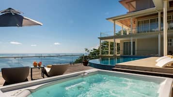 Una vasca idromassaggio con vista sull'oceano, una piscina e un edificio con un balcone.
