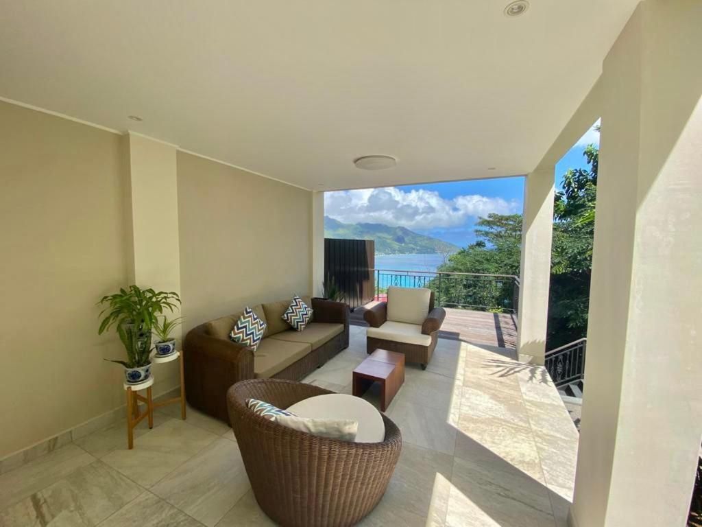 A spacious balcony with a view of the sea and mountains, furnished with a sofa, chairs, and a table.