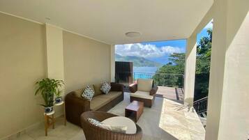 A spacious balcony with a view of the sea and mountains, furnished with a sofa, chairs, and a table.