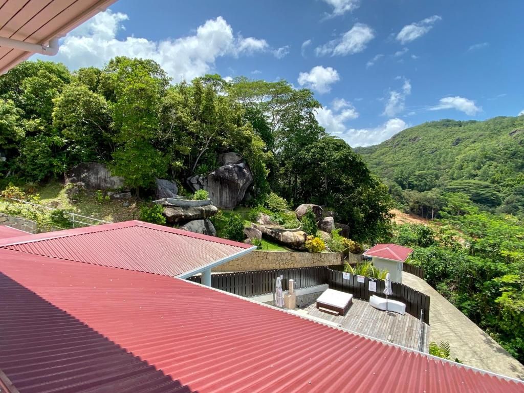 A rooftop terrace with a red roof, surrounded by lush greenery and a mountainous landscape.