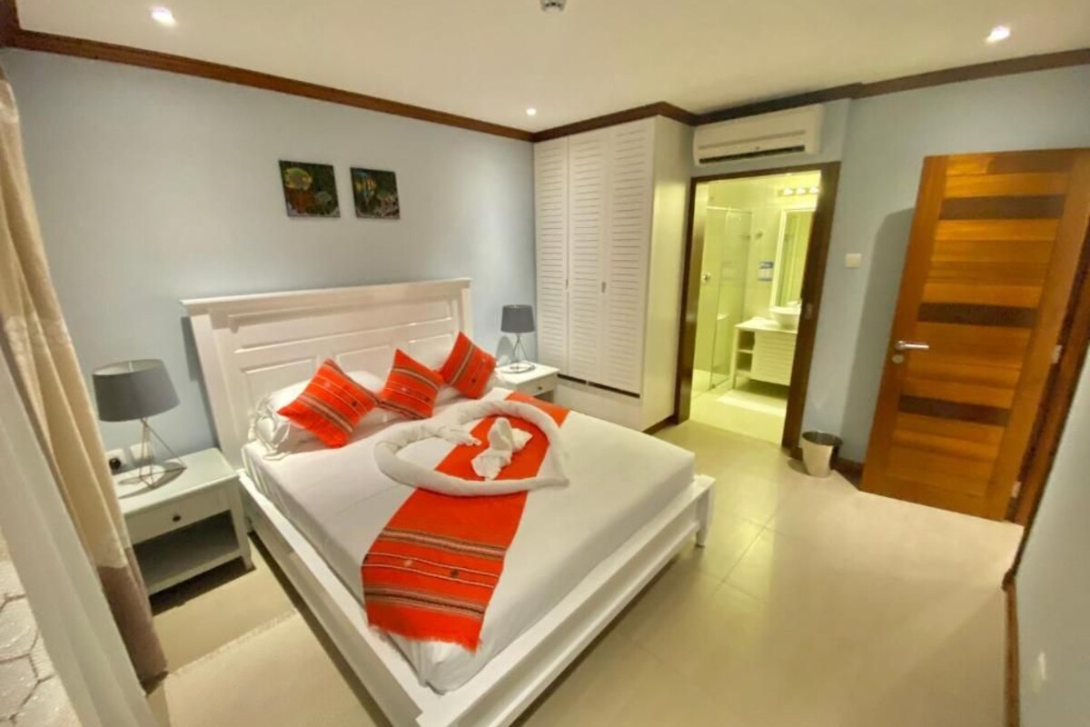 Une chambre d’hôtel avec un lit, une table de chevet et une salle de bain visible à travers une porte ouverte.