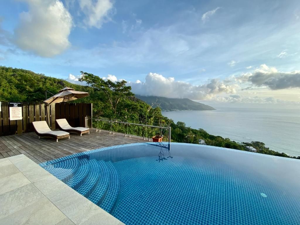 Une piscine à débordement offrant une vue sur la mer, des chaises longues et une terrasse en bois.