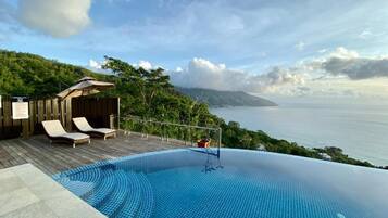 Una piscina infinita con vistas al mar, sillas de descanso y una terraza de madera.