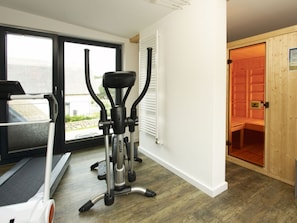 Ein Heimfitnessraum mit Trainingsgeräten, einer Glasschiebetür, die auf einen Balkon führt, und einem Saunabereich.