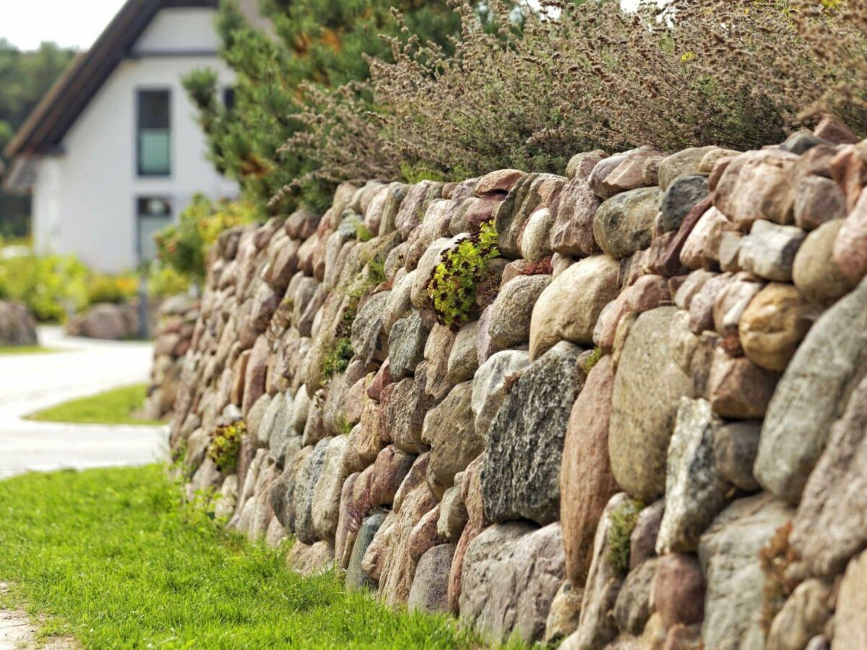 Un mur de pierre avec un chemin qui mène à un bâtiment.