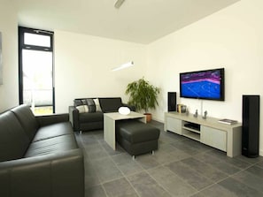 Ein modernes Wohnzimmer mit einer Couch, einem Couchtisch, einem Fernseher und einer Topfpflanze.