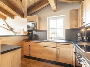 Una cocina con armarios de madera, encimera negra, una ventana y una cafetera.