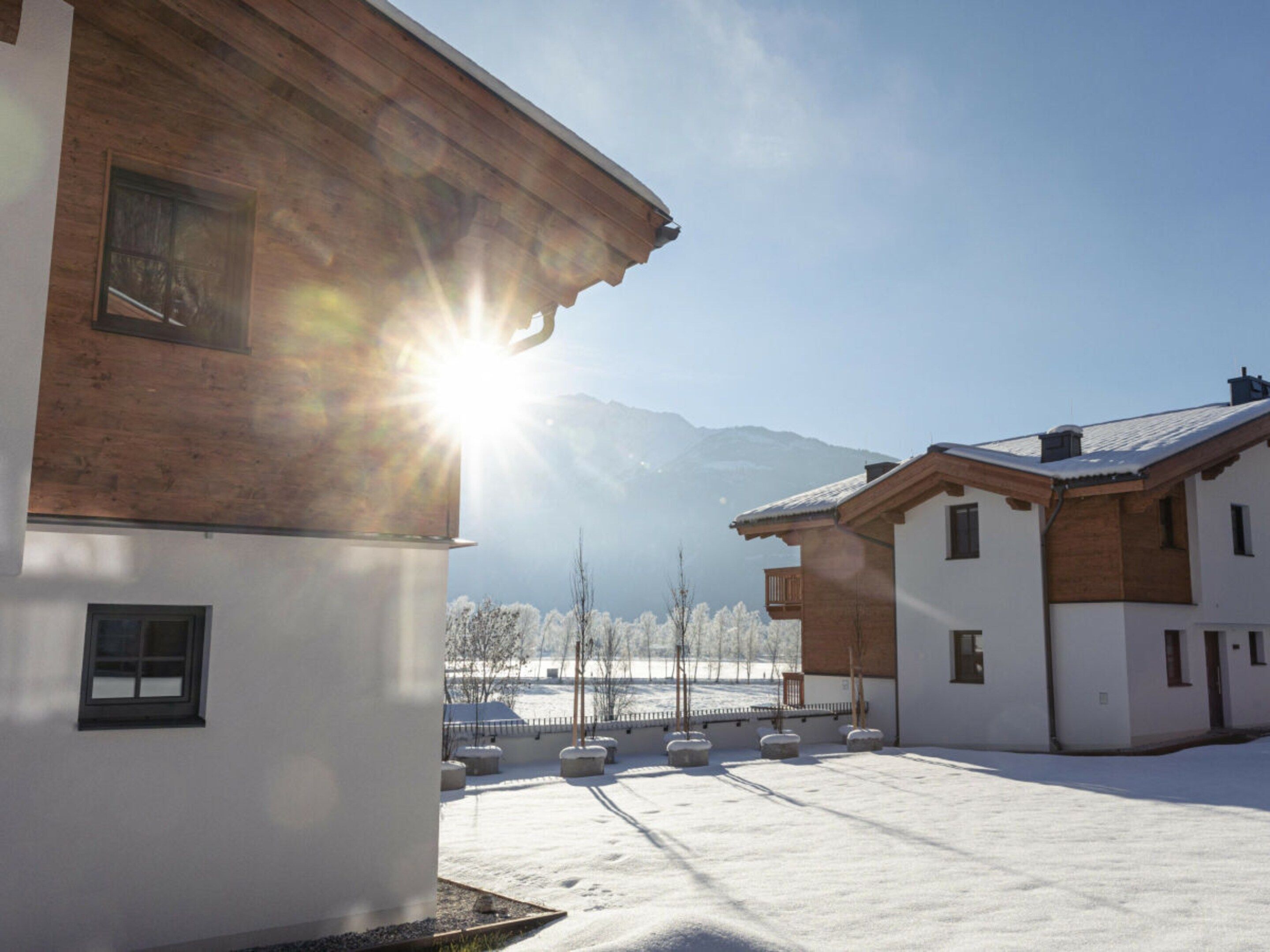 A snow-covered courtyard with buildings, a clear sky, and mountains in the background.