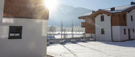 A snow-covered courtyard with buildings, a clear sky, and mountains in the background.