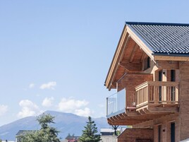 Un edificio de varios pisos con un balcón en el nivel superior, una montaña al fondo y un cielo despejado.