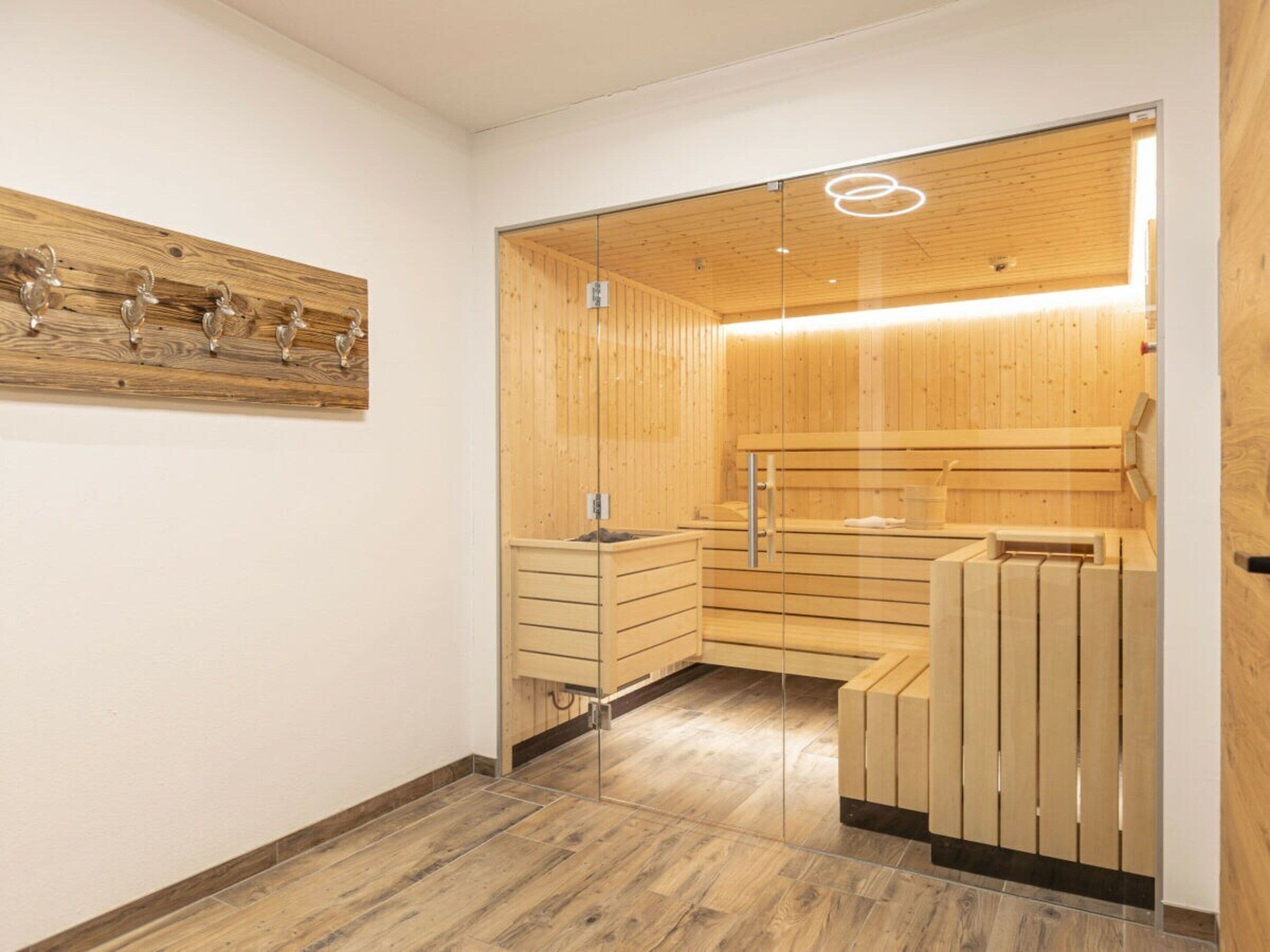 A sauna room with wooden walls and benches, a glass door, and a wooden ceiling.