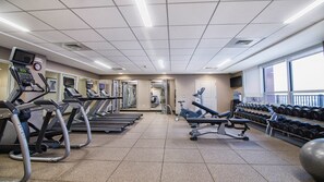 Une salle de sport équipée de tapis de course, de vélos elliptiques, d’un banc de musculation, d’haltères et de ballons d’exercice.