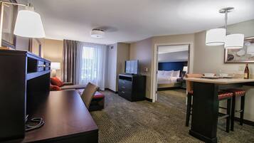 Quarto de hotel com escrivaninha, cadeira, cama, televisão e minibar.
