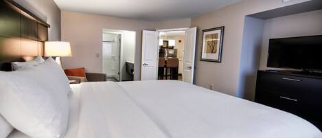 A hotel room with a large bed, a TV, a desk, and a bathroom visible through an open door.