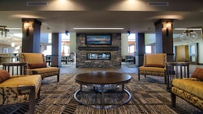A lobby with a stone fireplace, comfortable seating, and a large TV screen.