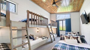 Une chambre avec des lits superposés, une échelle, un lit simple avec des oreillers, un ventilateur de plafond et un téléviseur fixé au mur.