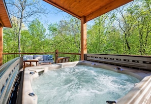 Ein Whirlpool unter einer Holzpergola mit Blick auf einen Wald.