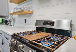 A kitchen with a stainless steel stove, a digital display, and a wooden shelf above it. - 2 Nearby Cabins | Private Heated Pool | Sleeps 34 (Broken Bow)