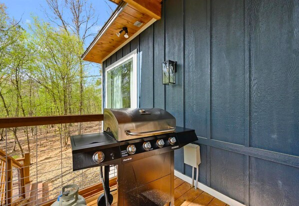 Una barbacoa a una terrassa exterior amb vista a arbres.