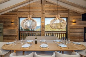 A wooden dining table set for six with a mountain view, two pendant lights, and a bottle of wine. - Chalet Montâme - Modern luxury in the Swiss Alps (Riddes)