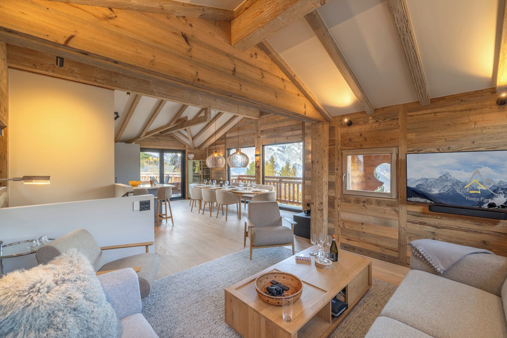 A wooden interior with a dining area, sofas, and a TV displaying a mountain view.