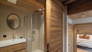A modern bathroom with a glass shower, wooden paneling, a round mirror, and a white sink. - Chalet Montâme - Modern luxury in the Swiss Alps (Riddes)