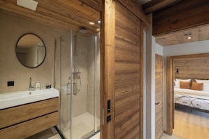 Un baño moderno con ducha de vidrio, paneles de madera, un espejo redondo y un lavamanos blanco.