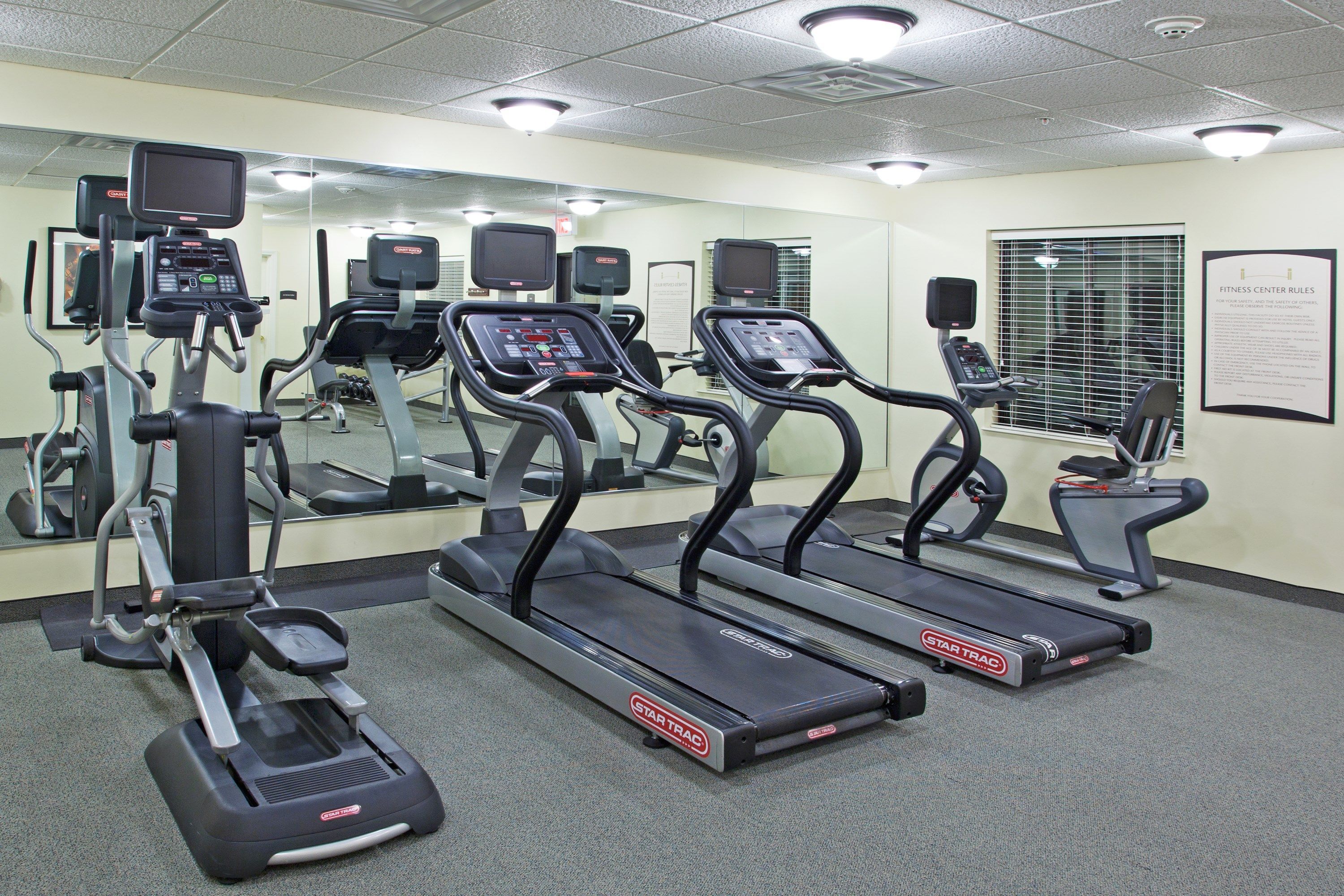 A fitness center with treadmills, elliptical machines, and a mirrored wall.