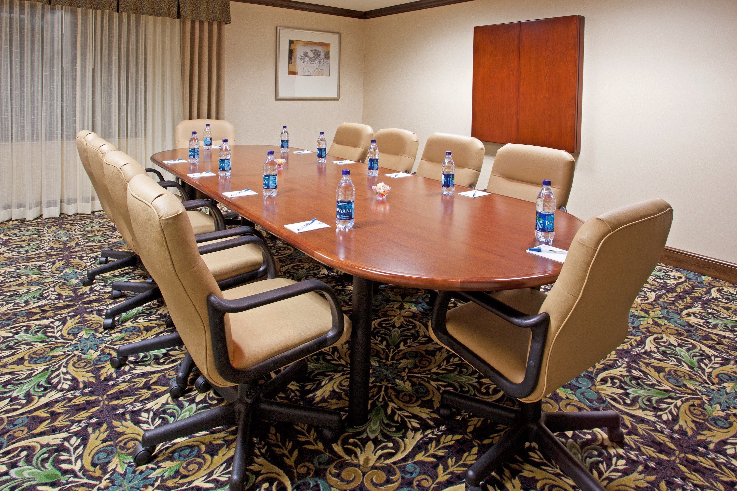 Un salón de conferencias con una gran mesa rodeada de sillas color beige, botellas de agua sobre la mesa y una alfombra estampada.