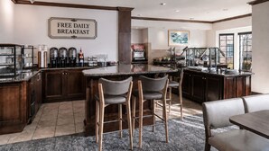 Een moderne keuken met een bar, een bord waarop aangegeven staat dat er dagelijks gratis ontbijt is, en een groot raam dat zorgt voor natuurlijk licht.