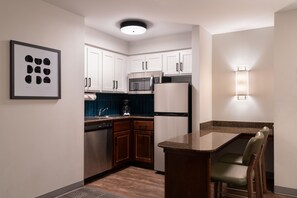 A modern kitchen with white cabinets, a microwave, a refrigerator, and a bar area with chairs.