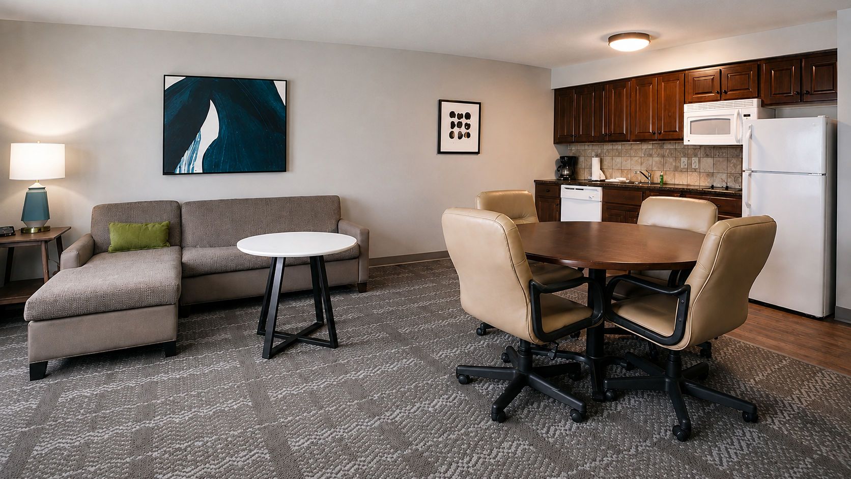 A modern living room with a sofa, a round coffee table, and a dining table with chairs. There is a kitchen area with cabinets and appliances.
