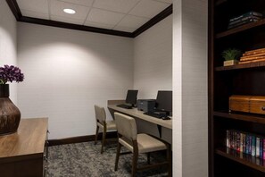 A corner office with two desks, chairs, a bookshelf, and a vase with flowers.