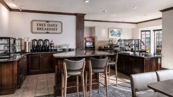 A modern kitchen with a bar area, a sign indicating free daily breakfast, and a large window providing natural light.