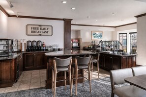 Una cocina moderna con barra, un letrero que indica desayuno diario gratuito, y un amplio ventanal que proporciona luz natural.