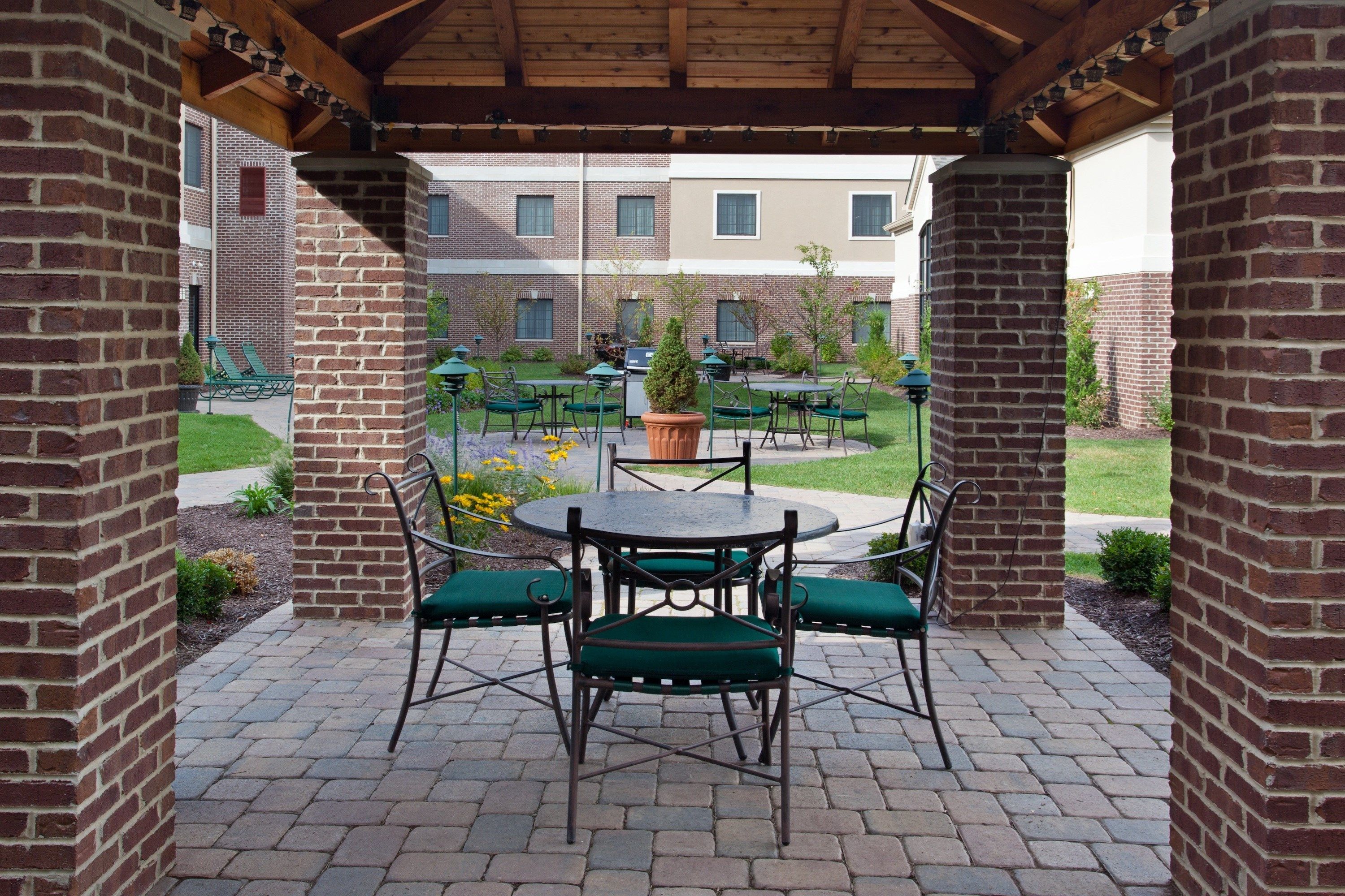 An outdoor patio area with brick pillars, green chairs, and a round table.