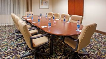 A conference room with a large table surrounded by beige chairs, water bottles on the table, and a patterned carpet.