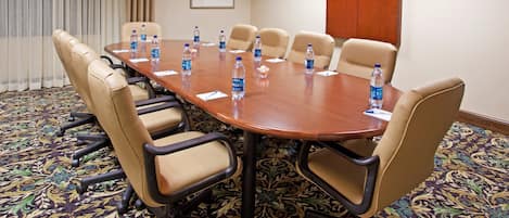 Une salle de conférence avec une grande table entourée de chaises beiges, des bouteilles d’eau posées sur la table et un tapis à motifs.
