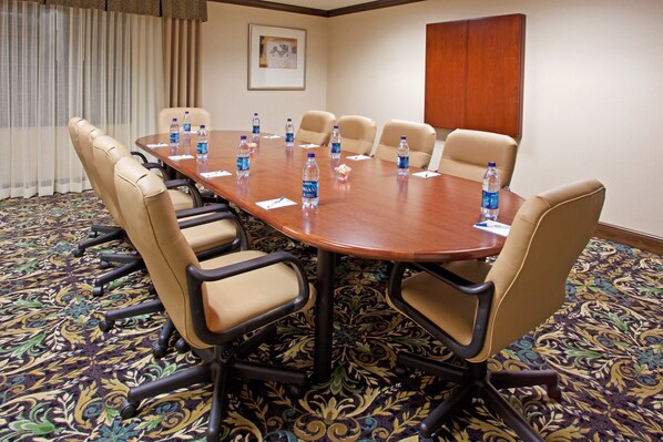 Un salón de conferencias con una gran mesa rodeada de sillas color beige, botellas de agua sobre la mesa y una alfombra estampada.