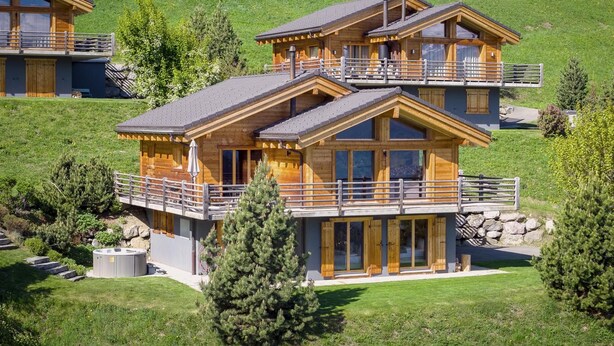 A multi-story chalet with balconies, large windows, and a stone foundation. - Chalet Aramis - Four Bedroom Chalet, Sleeps 8 (Riddes)