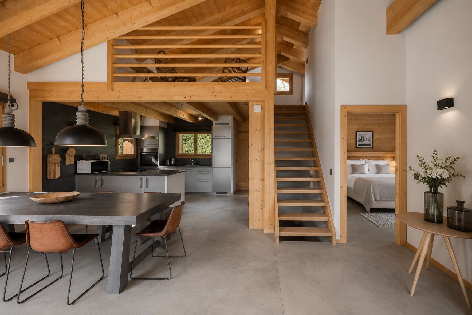 Un interior modern amb zona de menjador, cuina i escala que condueix a un dormitori tipus loft.