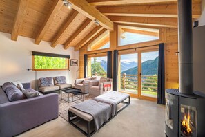 A cozy living room with a fireplace, wooden beams, and a balcony with a mountain view. - Chalet Aramis - Four Bedroom Chalet, Sleeps 8 (Riddes)