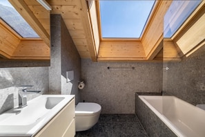 Un bany modern amb llum natural des del sostre, un vàter, una banyera i un lavabo.