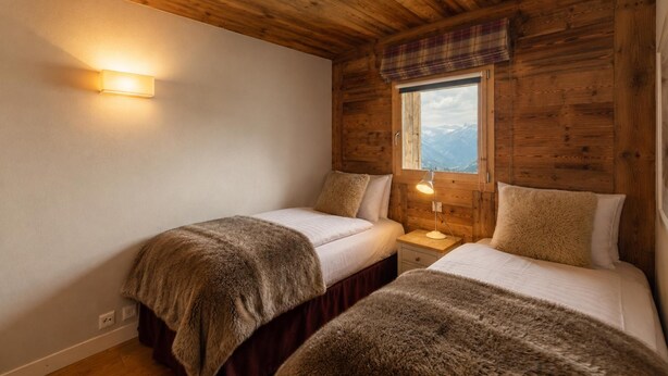 Una stanza con pareti in legno e una finestra vista montagne. Ci sono due letti con coperte soffici.