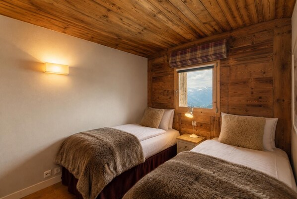 A room with wooden walls and a window with a view of mountains. There are two beds with fluffy blankets. - Chalet Big Bear - Five Bedroom Chalet, Sleeps 10 (Riddes)