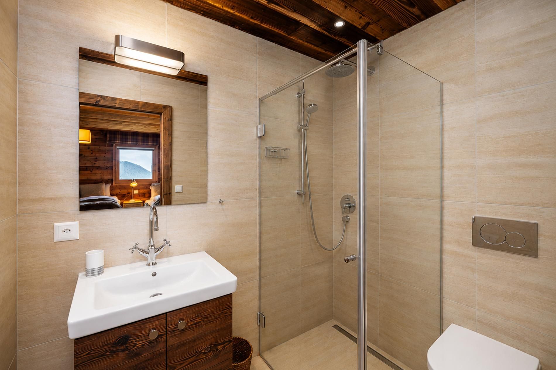 A bathroom with a glass shower enclosure, a sink with a mirror above, and a wooden vanity.