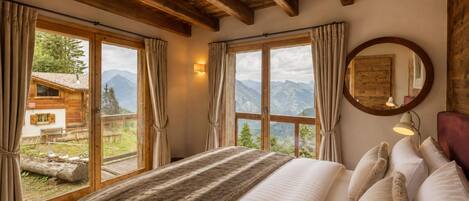 Un dormitorio con una cama grande, vigas de madera, vistas a montañas y una cabaña de madera en el exterior.