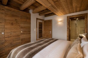 Une chambre avec des lambris en bois, un lit recouvert d’une couverture à rayures et un espace douche.